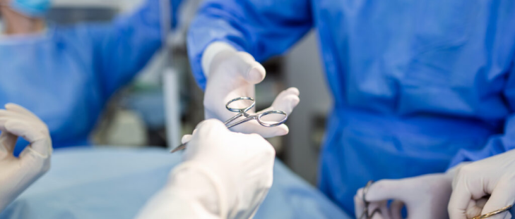 doctor vistiendo ropa quirúrgica recibiendo unas tijeras de su asistente