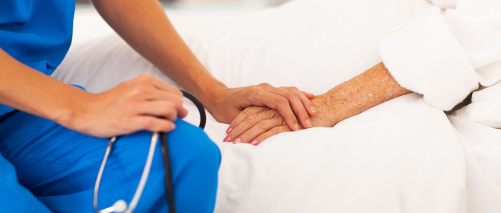 medico vistiendo ropa color azul sosteniendo la mano de un paciente acostado en una cama.